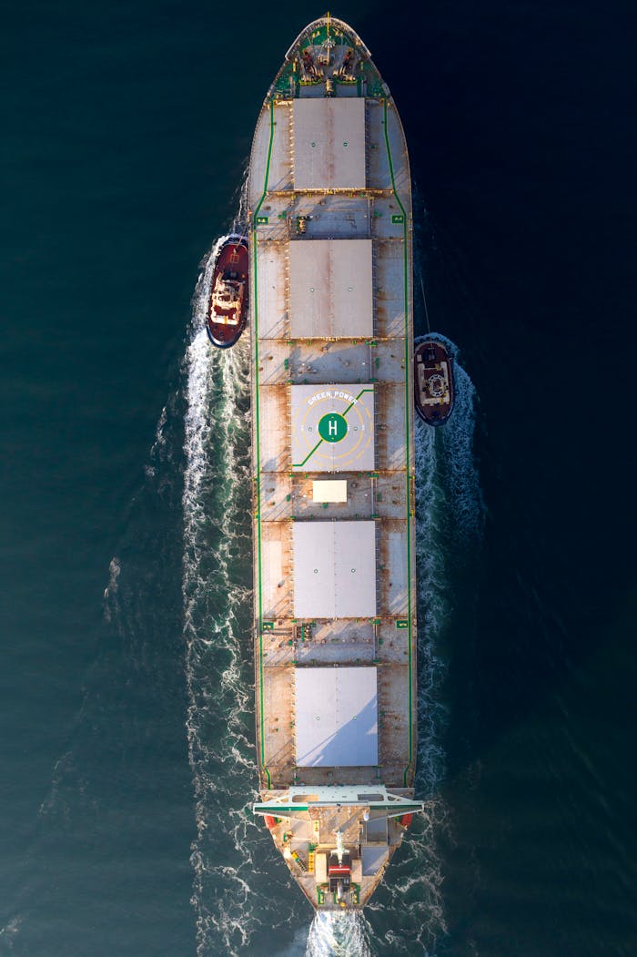An aerial photo of a large cargo ship with tugboats assisting in open sea, showing maritime transportation.