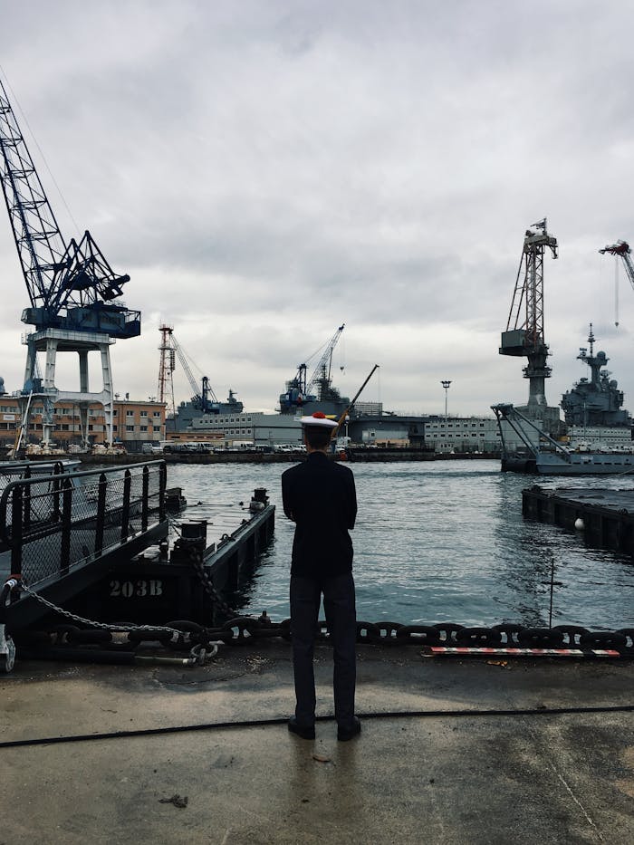 Navy officer oversees ships at Toulons industrial harbor under a cloudy sky.